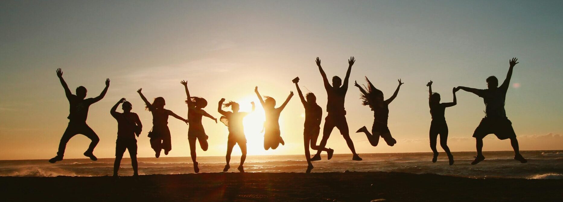 Silhouette of a group of friends jumping on a beach at sunset, expressing joy and freedom.